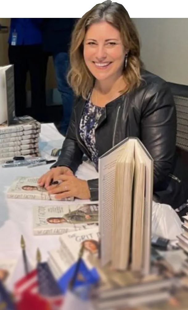Woman signing books at a table with stacks of books around her.