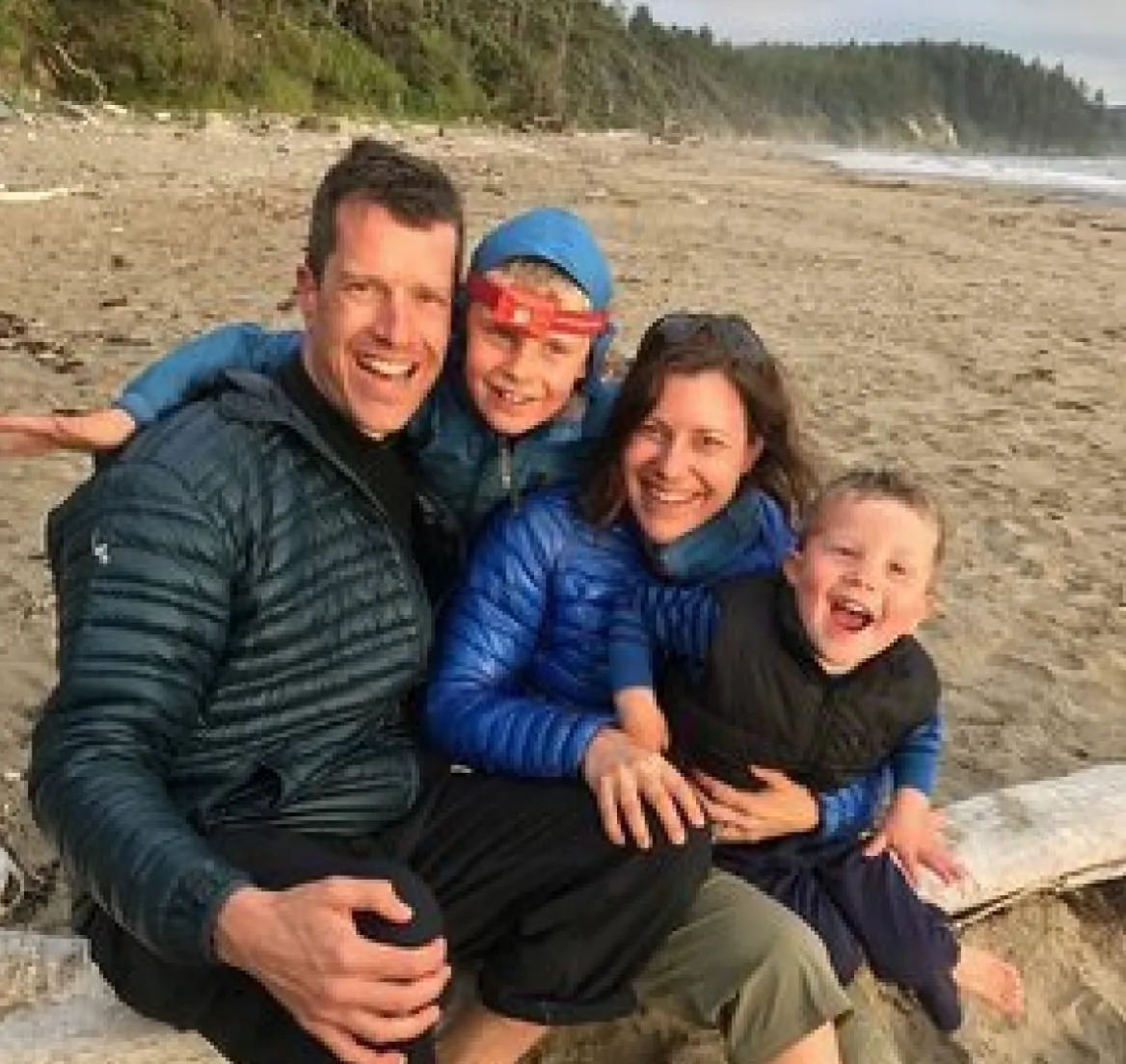 Family sitting together on a beach, smiling at the camera
