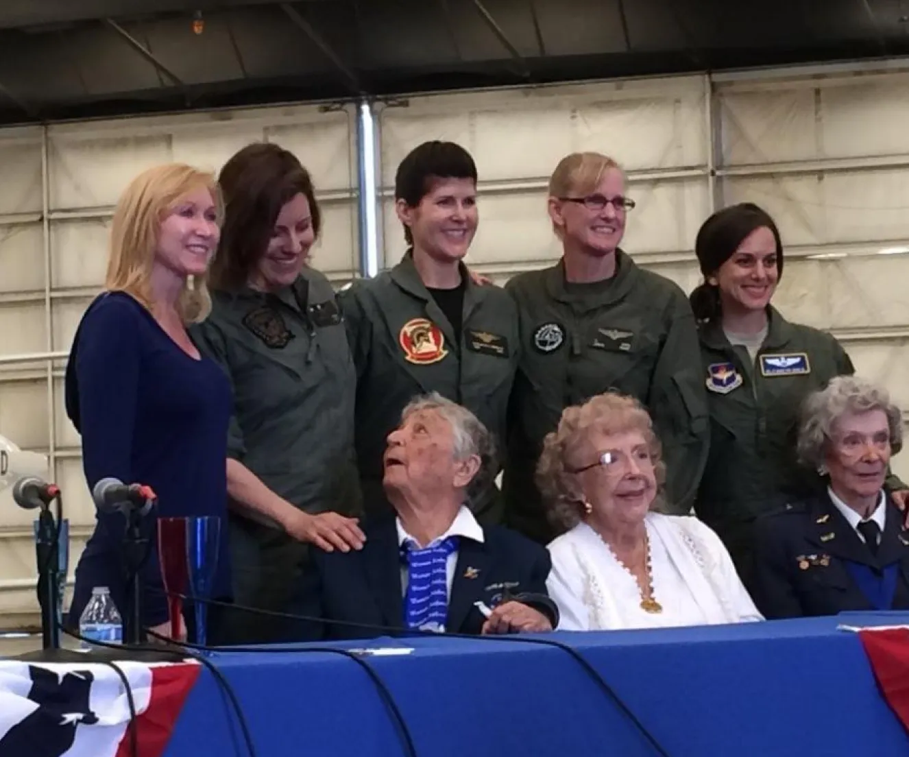 Group photo of women in military flight suits with elderly veterans