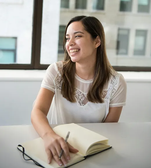 Woman smiling while writing in a notebook at a desk