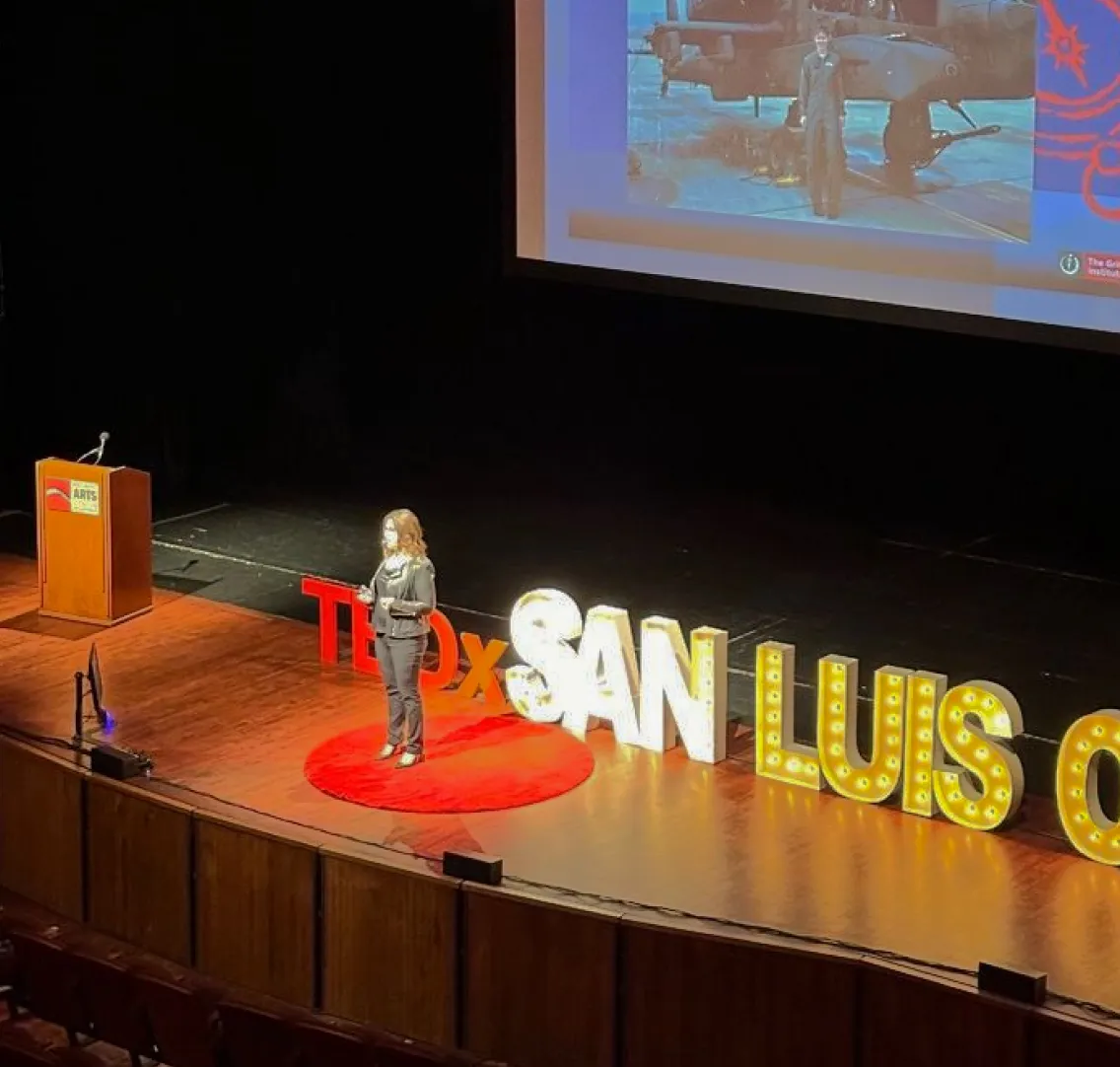 Speaker standing on a TEDx stage with a large presentation screen
