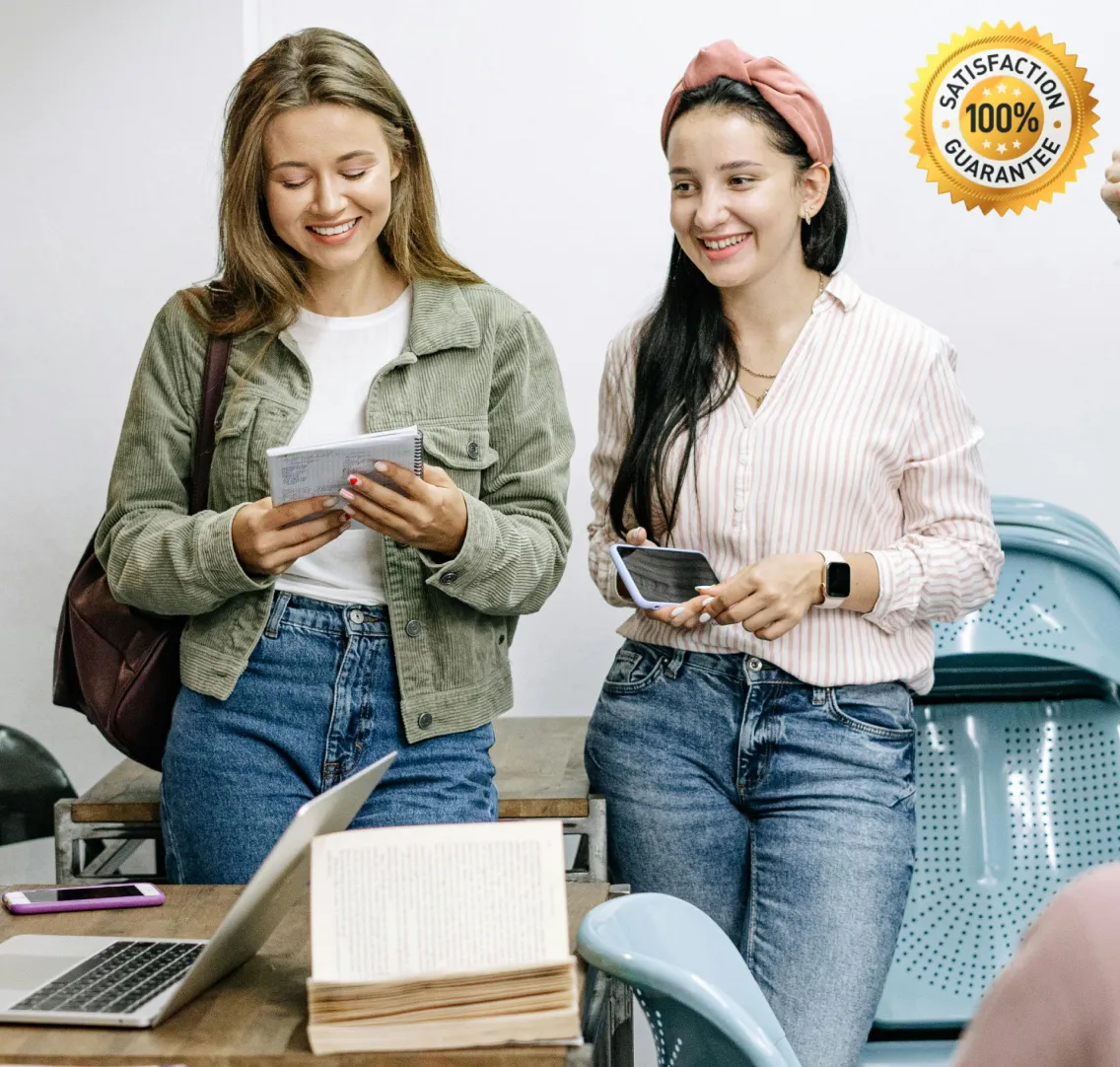 Two women smiling and holding notebooks in a classroom