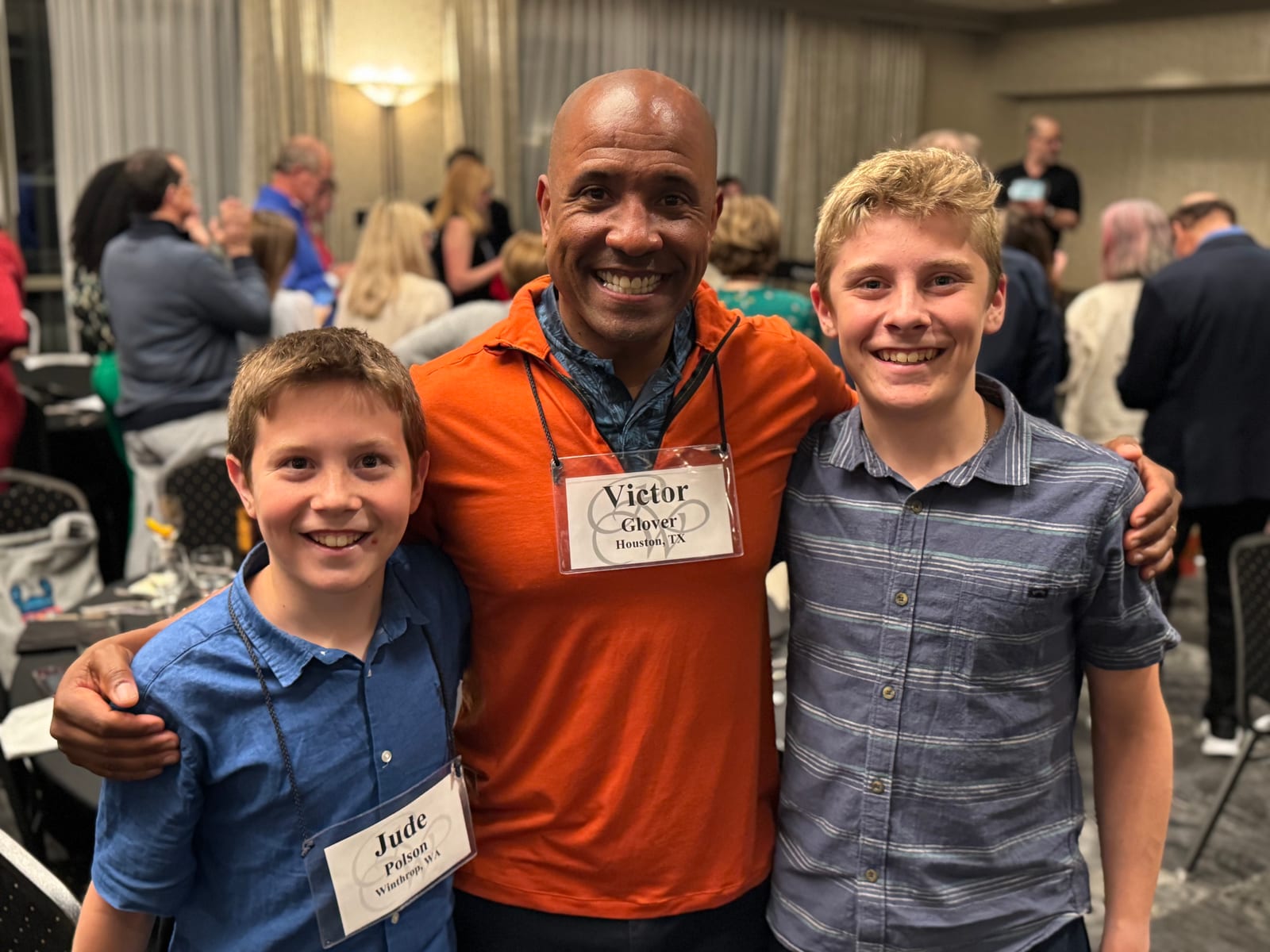 Two boys with name tags pose with a guest at an event