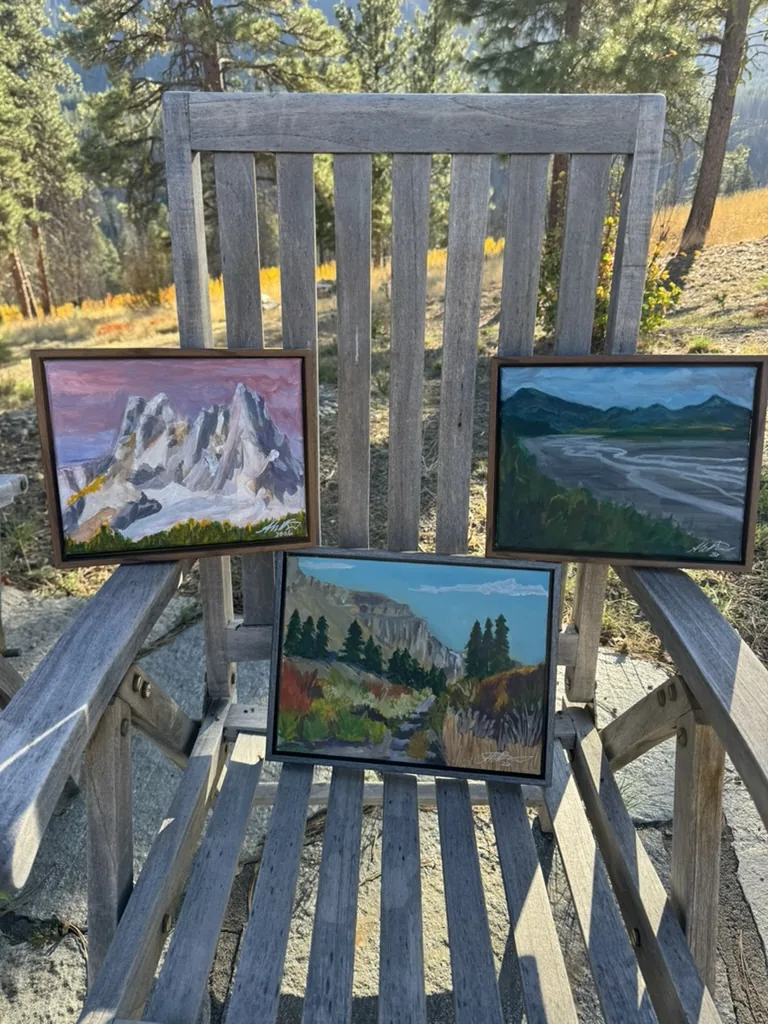 Three of Shannon Huffman Polson&rsquo;s landscape paintings on a wooden bench among the pines